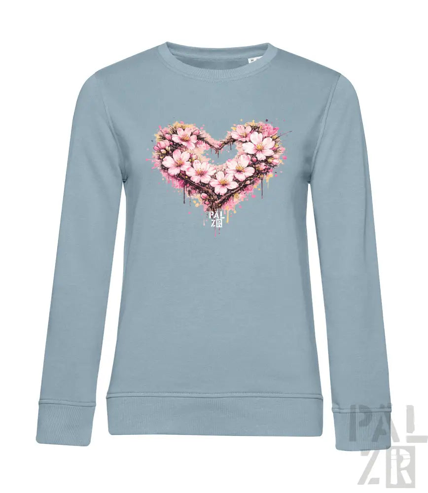 Ein hellblaues Langarm-Sweatshirt mit einem lebendigen herzförmigen Blumendesign aus pinken und weißen Blüten mit Spritzeffekten.