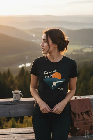 Schwarzes T-Shirt mit einem grafischen Druck einer orangenen Sonne über Bergen und dem deutschen Spruch ’da wo ich her bin’ in weißer Schrift, mit einem kleinen Palz-Logo unten rechts.