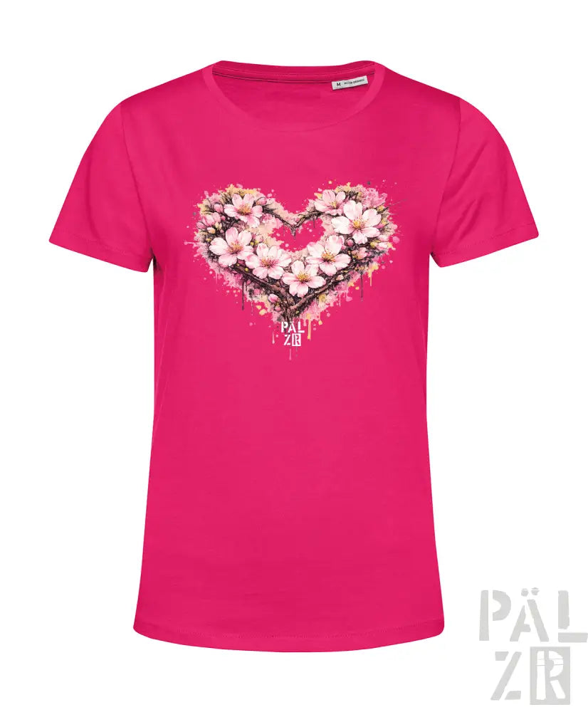 Ein lebhaftes rosa Damen-T-Shirt mit einem herzförmigen Blumenmuster, das zarte Blüten und Spritzeffekte aufweist.