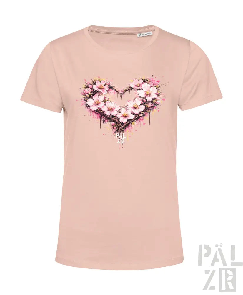 Ein weiches rosa Damen-T-Shirt mit einem lebendigen herzförmigen Blumenmuster, das zarte Blüten und Spritzfarben-Akzente aufweist.
