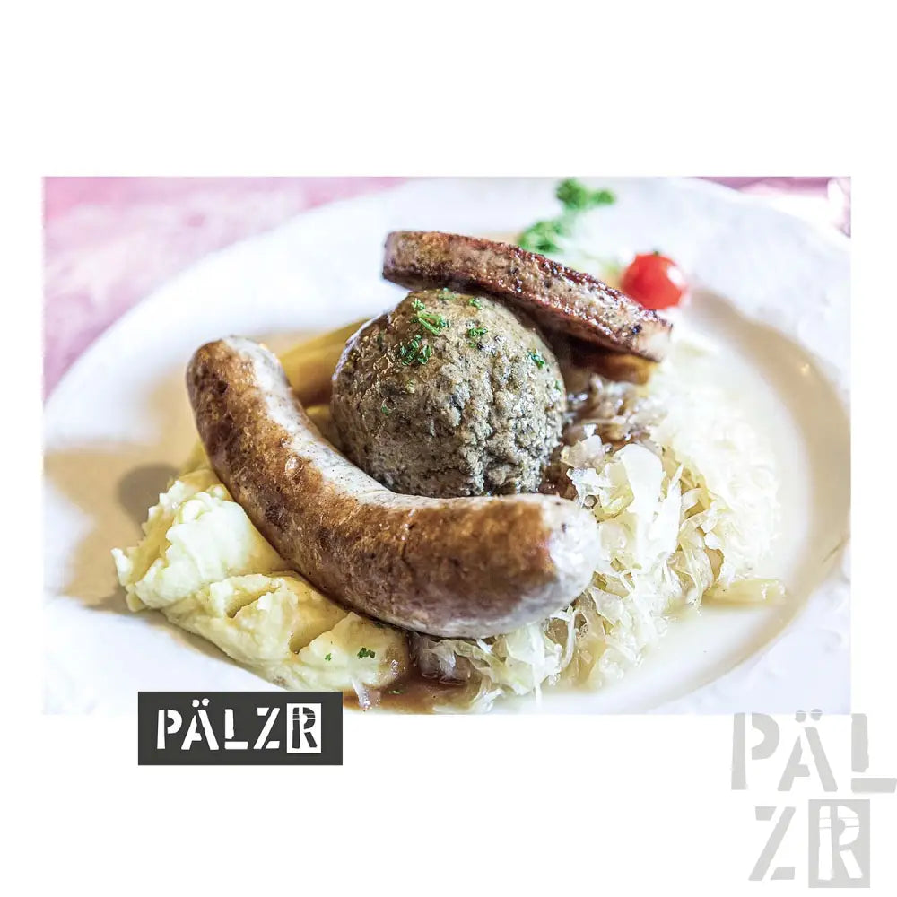 Weißer Teller mit Würsten und Kohl, belegt mit einem grünen Kräuterbällchen.