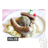 Weißer Teller mit Würsten und Kohl, belegt mit einem grünen Kräuterbällchen.
