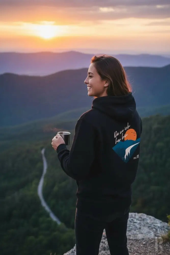 Schwarzes Hoodie mit einem farbenfrohen Grafikmotiv einer orangenen Sonne über Bergen und dem Text „do we see her love“ auf der Rückseite.