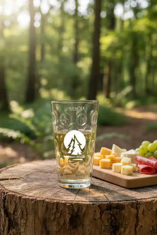 Klares Glas-Pint-Glas mit geprägten kreisförmigen Mustern und einem weißen Logo, das Berge und darunter das Wort 'palz' zeigt.
