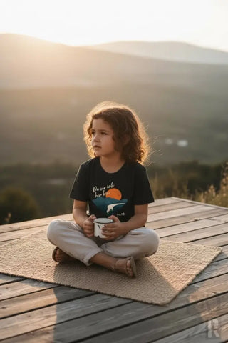 Schwarzes T-Shirt mit einem Sonnenuntergang- und Berg-Grafikdesign, das weißen Text oberhalb des Bildes aufweist