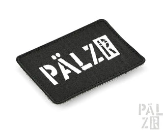 Schwarzer rechteckiger Aufnäher mit weißem Text und Design, wahrscheinlich aus Stoff oder synthetischem Material gefertigt.