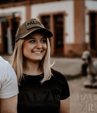 Olivgrüner Baseballcap mit „pälzb“-Text und schwarzem T-Shirt.