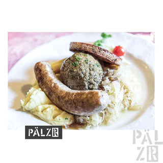 Weißer Teller mit Würsten und Kohl, belegt mit einem grünen Kräuterbällchen.