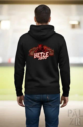 Schwarze Kapuzenjacke mit einem rot-weißen Grafikmotiv eines Teufels und dem Text „betze 1900“ darunter.