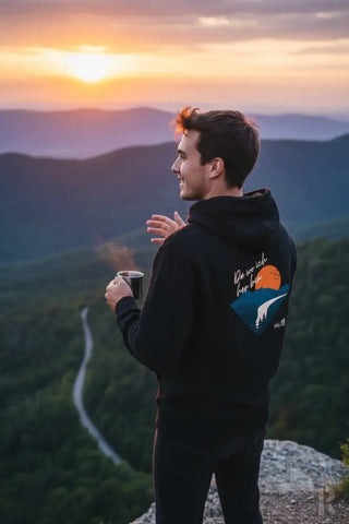 Schwarze Kapuzenjacke mit einem farbenfrohen Grafikdesign auf dem Rücken, das eine orange Sonne und eine weiße Bergsilhouette zeigt.