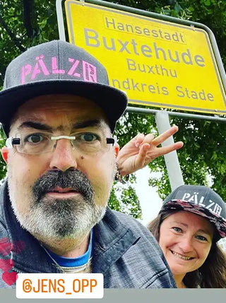 Ein Mann und eine Frau machen ein Selfie vor einem gelben Ortsschild.