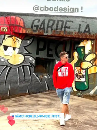 Mann in einem roten Hoodie, hellblauen Jeansshorts und weißen Turnschuhen.