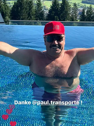 Lächelnder Mann mit Schnurrbart, Sonnenbrille und roter Baseballmütze im Swimmingpool.