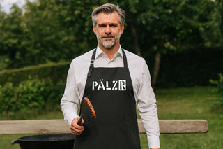 Ein Mann in einem weißen Hemd und einer schwarzen Schürze, der eine Wurst mit Zangen hält.