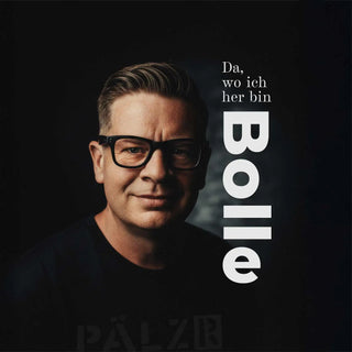 Ein Mann mit ordentlich gestyltem grauem Haar und schwarzem Gestell-Brille, der ein dunkles Hemd trägt.