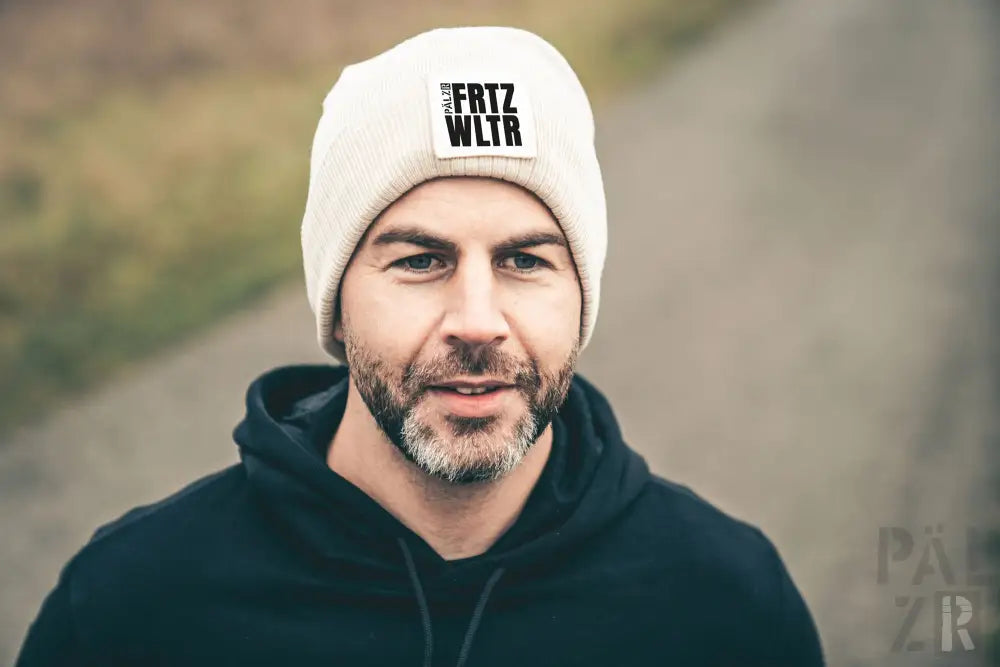 Weiße Beanie mit schwarzem Text ’frtz wltr’ und Logo, wahrscheinlich aus Wolle oder Acryl.