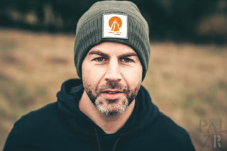 Graue Beanie mit orangem und weißem Logo, wahrscheinlich Wolle- oder Acryl-Mischung.