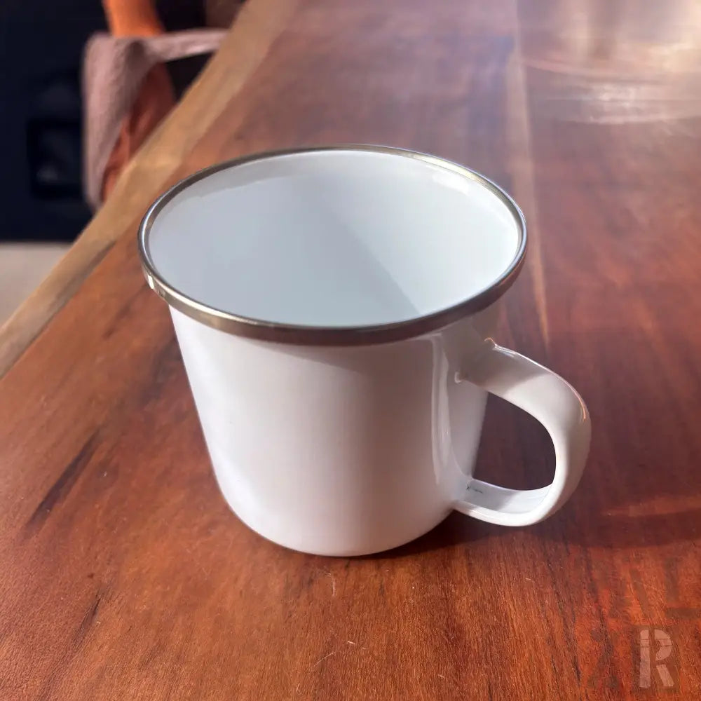 Weißer Emaille-Becher mit silbernem Rand und Griff, rustikales Design.