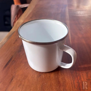 Weißer Emaille-Becher mit silbernem Rand und Griff, rustikales Design.