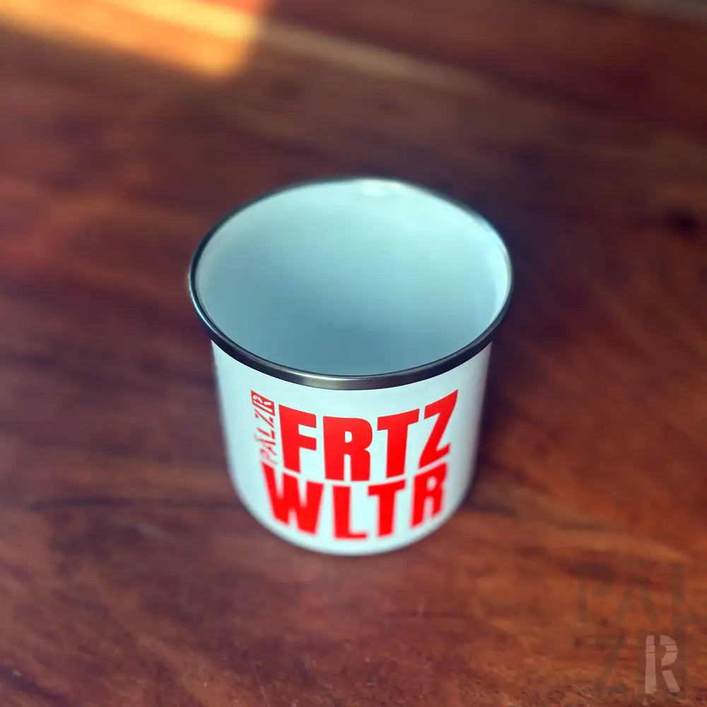 Weißer Emaillebecher mit rotem Text „frtz wltr“ und schwarzem Rand, auf Holzoberfläche platziert.