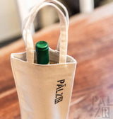 Cremeweiße Leinwand-Weintasche mit schwarzer ’palzr’-Markierung und grüner Flasche darin.