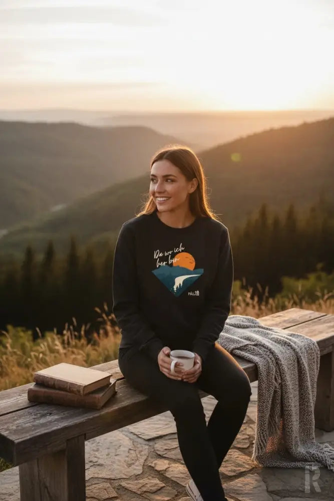 Schwarzes langärmeliges Sweatshirt mit einem Grafikdruck eines Sonnenuntergangs über Bergen und dem Text ’we are rich for love’ darüber, mit einem kleinen Logo auf dem unteren rechten Ärmel.