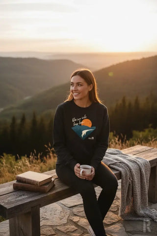 Schwarzes langärmeliges Sweatshirt mit einem Grafikdruck eines Sonnenuntergangs über Bergen und dem Text ’we are rich for love’ darüber, mit einem kleinen Logo auf dem unteren rechten Ärmel.