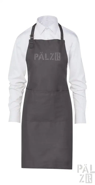 Dunkelgraue Schürze aus Kohle mit verstellbarem Nackenschnur und Vordertasche, mit dem ‚palzr‘-Logo.