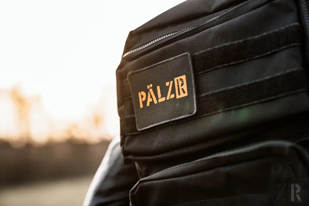 Schwarzer taktischer Rucksack mit goldenem ’pälzr’-Logo und Reißverschlussdetails.