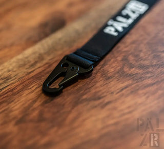 Schwarzes Band mit Text ’palzr’ und Karabinerclip, Nylon-Material.