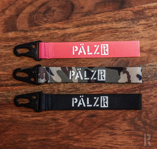 Palzr-markierter Lanyard mit Tarn- und Pink-Farboptionen, ausgestattet mit einer schwarzen Plastikclip.