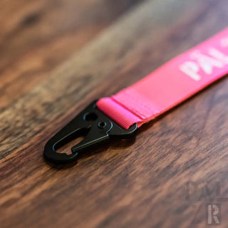Neonpinker Lanyard mit schwarzer Clips und weißem Text „pan“ auf Holzoberfläche.