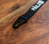 Schwarzes Band mit Text ’palzr’ und Karabinerclip, Nylon-Material.