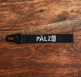 Schwarzes Lanyard aus Filz mit weißem Logo und Metallhaken.