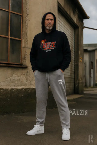 Schwarzer Hoodie mit rot-weißem Logo, graue Jogginghose, weiße Sneaker.