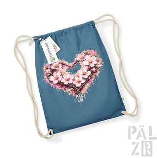 Eine türkisfarbene Beutel mit Kordelzug, die ein lebendiges, pinkfarbenes Kirschenblüten-Herz-Design mit Spritzeffekten und dem Text „pal zib“ darunter zeigt.