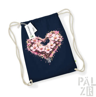 Eine marineblaue Beutel mit Kordelzug, die ein lebendiges, pinkfarbenes Kirschblüten-Herz-Design mit Spritzeffekten und dem Text „pal zib“ darunter aufweist.