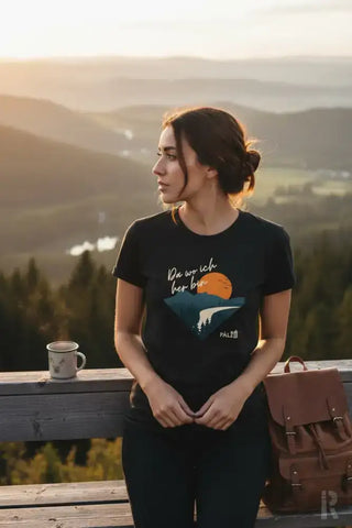 Schwarzes T-Shirt mit einem grafischen Druck einer orangenen Sonne über Bergen und dem deutschen Spruch ’da wo ich her bin’ in weißer Schrift, mit einem kleinen Palz-Logo unten rechts.
