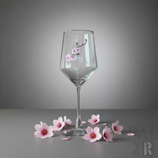 Ein klares Glas-Weinglas, verziert mit zartem rosa Kirschblüten-Kunstwerk an seiner Seite.