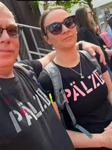 Zwei Personen tragen passende schwarze T-Shirts mit einem deutschen Wort und tragen Rucksäcke