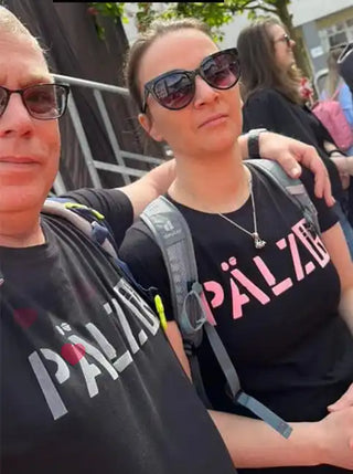 Zwei Personen tragen passende schwarze T-Shirts mit einem deutschen Wort und tragen Rucksäcke